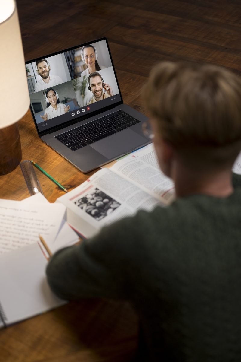 A student writing in a notebook while video-calling a tutor